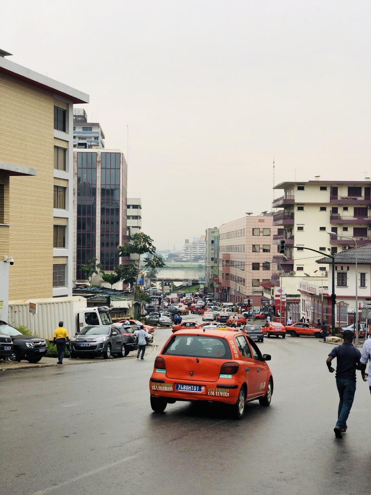 Orangefarbenes Taxi auf einer Straße in Abidjan mit weiteren Taxis im Hintergrund