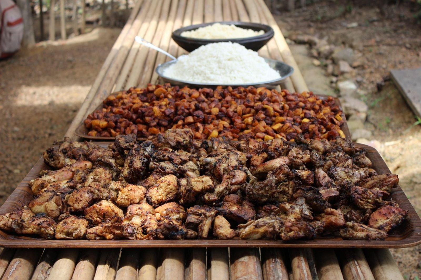 Große Platten mit gegrilltem Fleisch, Reis und Alloco auf einem Holztisch