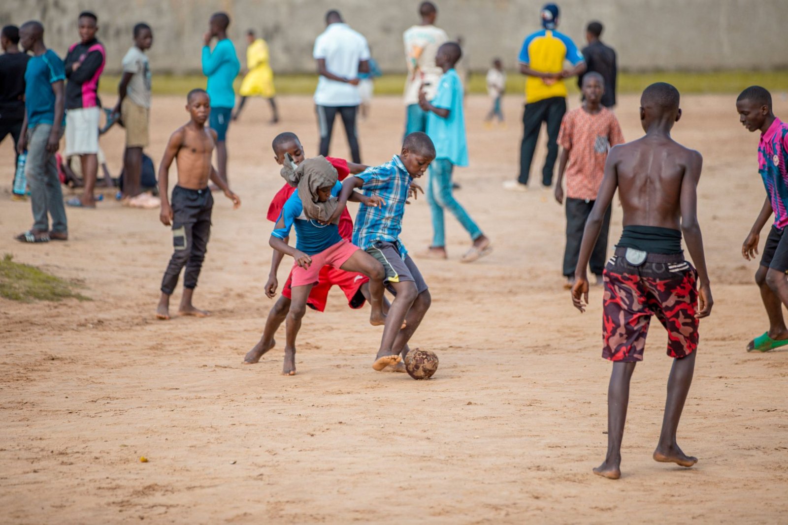 Kinder spielen barfuß Fußball auf einem Sandplatz