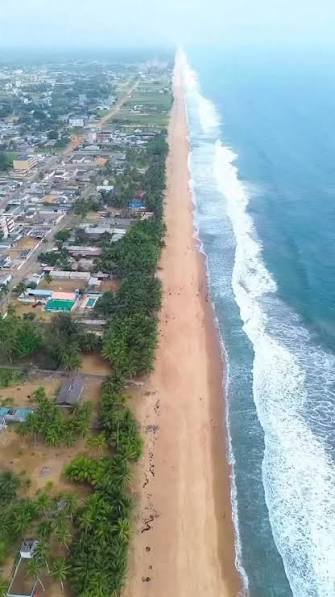 Luftbild einer langen Sandküste mit Ort und Palmenreihe am Atlantik