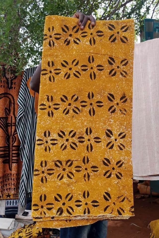 Gelbes Korhogo-Tuch mit dunklen Blütenmotiven, hochgehalten