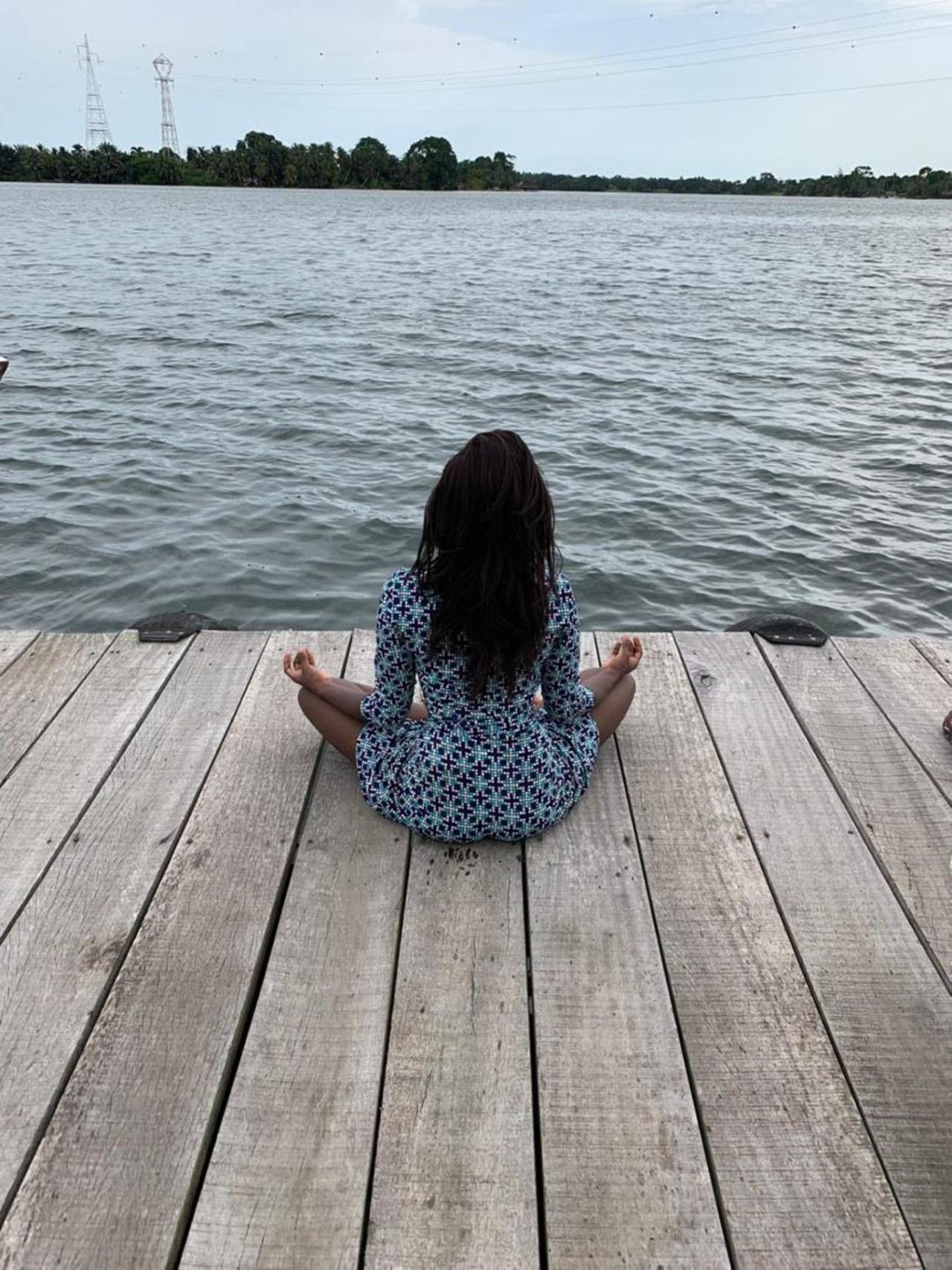 Frau sitzt auf einem Holzsteg am ruhigen Lagunenwasser