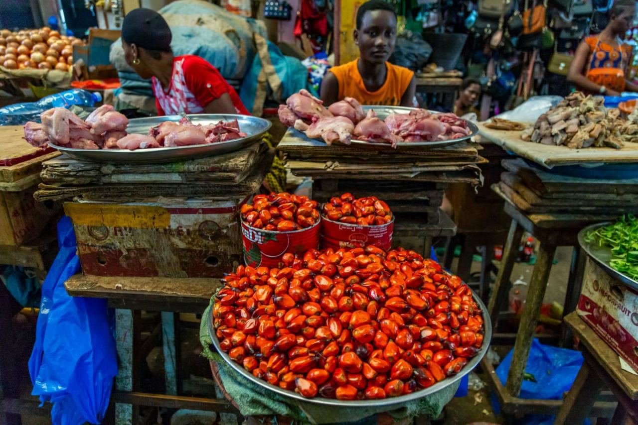 Marktstand mit Schalen voller roter Ölpalmnüsse und Geflügel