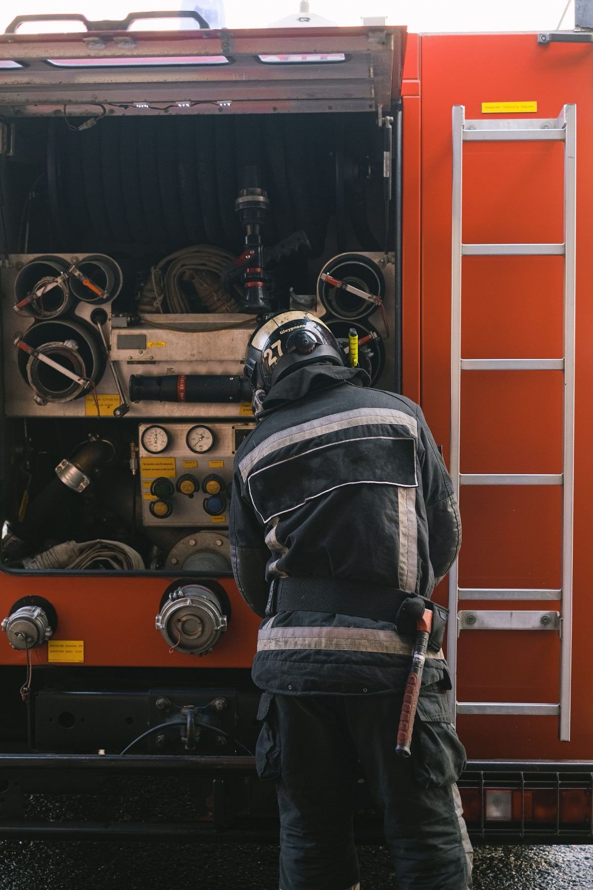 Feuerwehrmann von hinten vor dem geöffneten Geräteraum eines Löschfahrzeugs