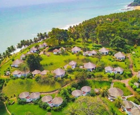 Luftbild einer Anlage mit Rundhütten auf einer grünen Landzunge am Meer