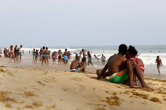 Belebter Strand mit Badenden, im Vordergrund ein sitzendes Paar