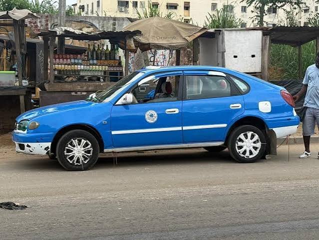 Blaues Sammeltaxi am Straßenrand vor einem Kiosk