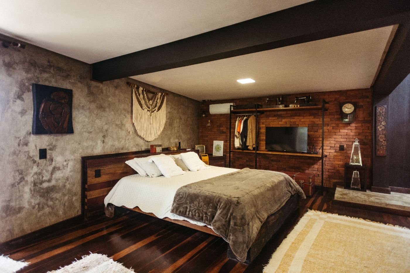 Schlafzimmer mit großem Bett, Wänden aus Sichtbeton und Ziegel, Klimaanlage an der Wand