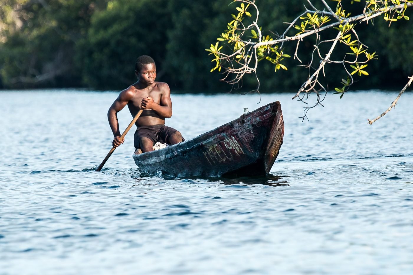 Junger Mann paddelt eine Piroge über stilles Lagunenwasser